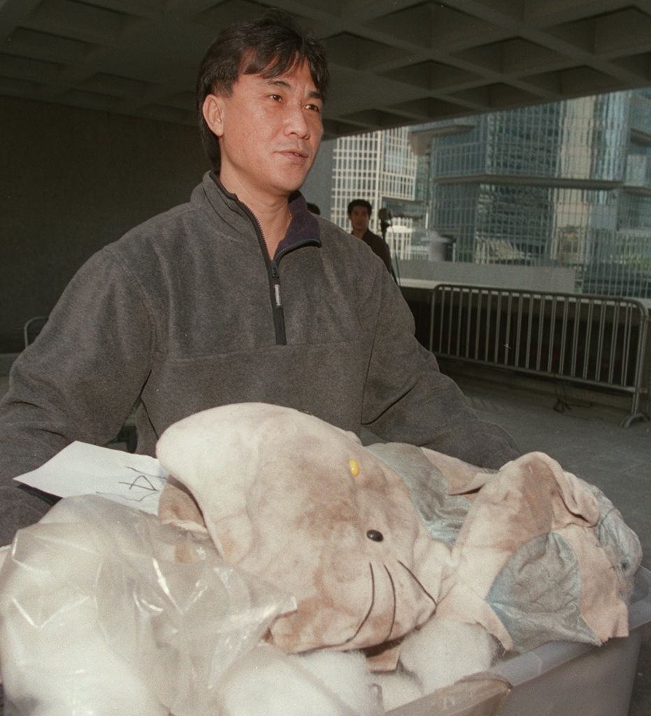 En person med et alvorlig uttrykk håndterer en stor utstoppet elefant, med bygninger i bakgrunnen