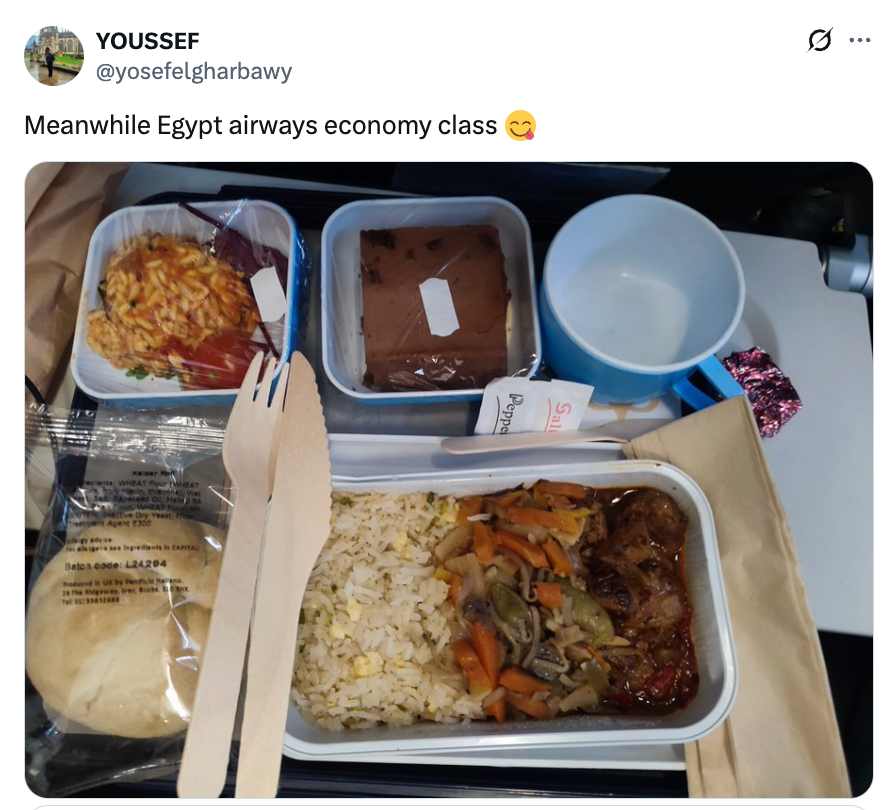 Flymåltid med ris, grønnsaker, kylling, rundstykke og dessert på et brett, akkompagnert av trebestikk, servert på Egypt Airways økonomiklasse