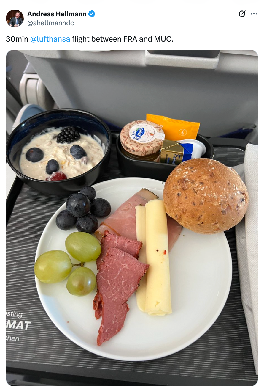 Flymåltid med yoghurt, bær, kjøttpålegg, ost, rull, smør og drikkevarer på et brett under en kort Lufthansa-flyvning