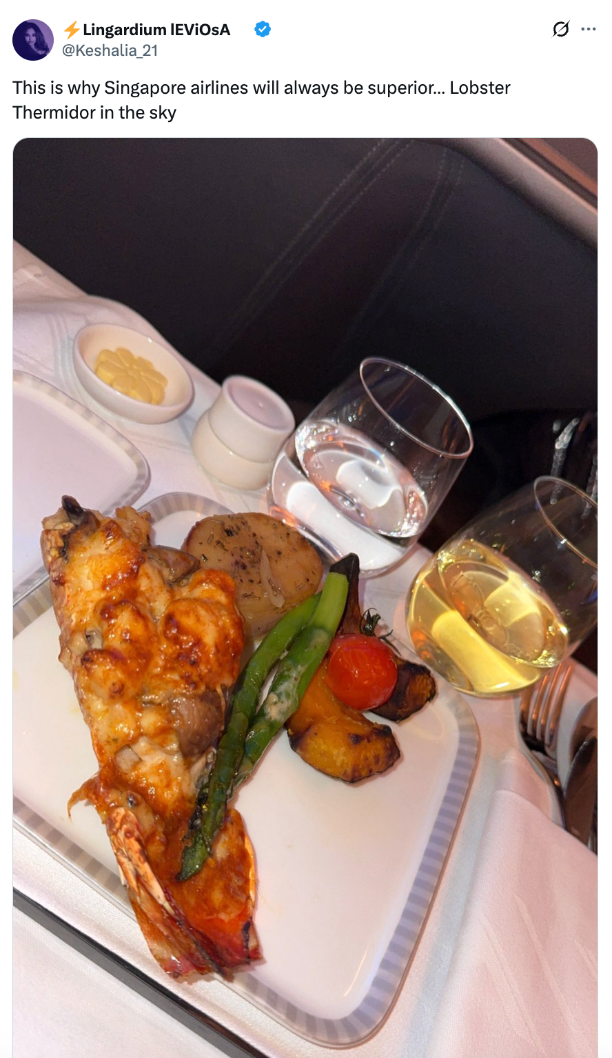 Belagt Hummer Thermidor med ristede grønnsaker på et brett i en flyservering, akkompagnert av en rundstykke, smør og drinker