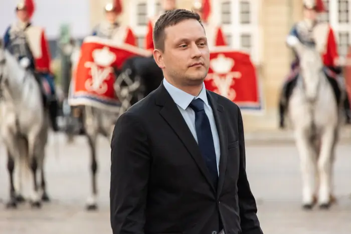 En person i dress står foran seremonielle vakter på hesteryggen, med dekorative uniformer med emblemer