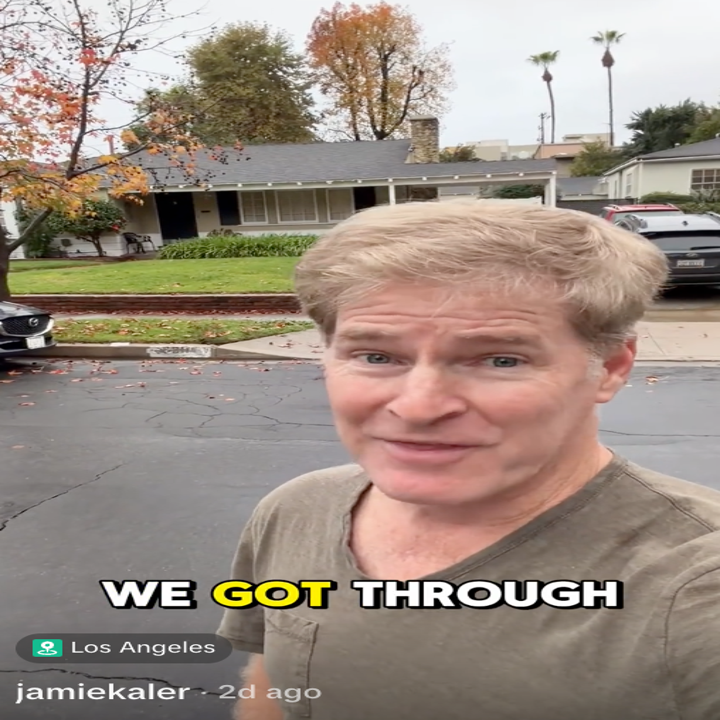 En person som smiler utendørs på en gate, med et hus og trær i bakgrunnen. Teksten lyder "WE GOT THROUGH" med beliggenhet merket som Los Angeles