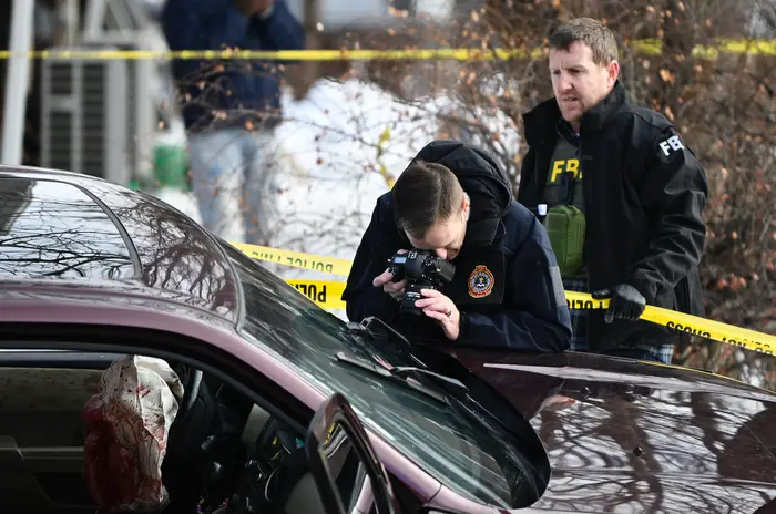 FBI-agenter undersøker et åsted nær en bil med knuste vinduer, gul forsiktighetstape rundt. En agent fotograferer bevis
