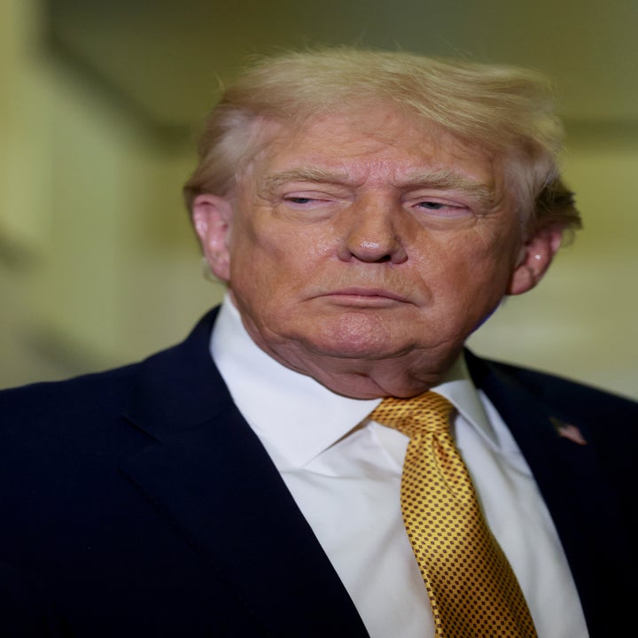 En person i dress og slips ser til siden med et nøytralt uttrykk innendørs