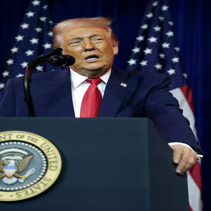 En person på et podium snakker i en mikrofon, med flere amerikanske flagg i bakgrunnen