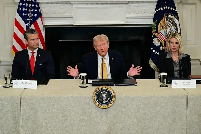 Tre personer sitter ved et konferansebord med mikrofoner, med presidentsegl utstilt i bakgrunnen