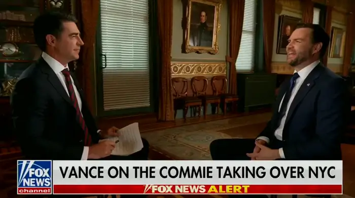 To menn i dress diskuterer et emne på et nyhetsprogram. Skjermen viser overskriften: "Vance on the Commie Taking Over NYC."