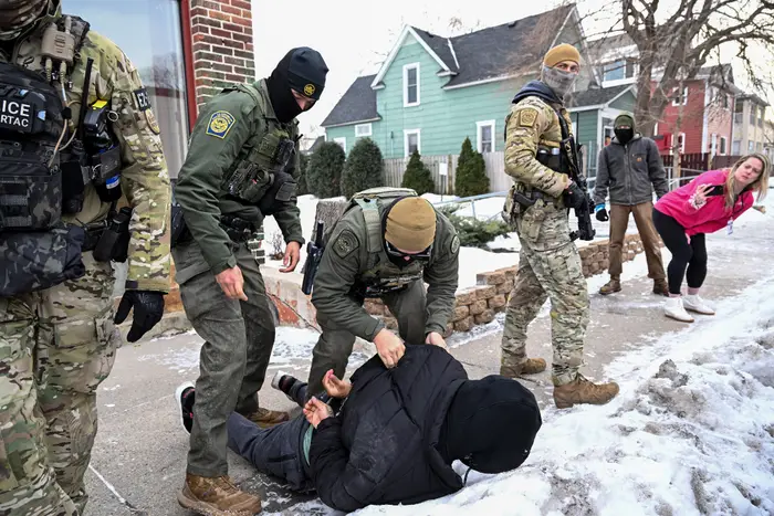 Politifolk holder tilbake en person på et snødekt fortau mens andre observerer i nærheten