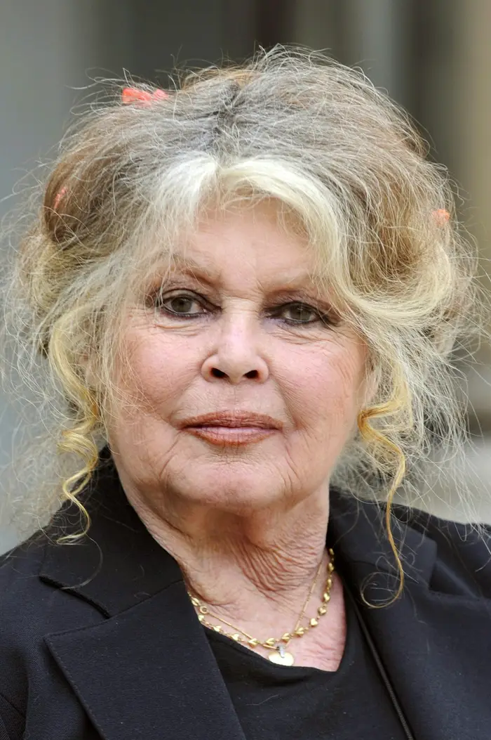 To individer er side om side i formell antrekk. Til venstre en person med bølget hår og et halskjede; til høyre en person med kort hår og skjorte med krage