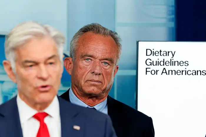 To menn i dress på en pressekonferanse. En skjerm viser "Dietary Guidelines for Americans" i bakgrunnen