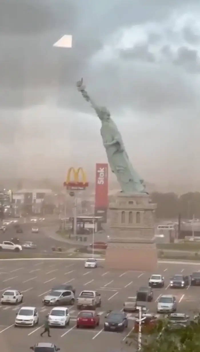Statue of Liberty-replika på en sokkel på en parkeringsplass, nær McDonald's og Sock-butikkskiltene. Overskyet himmel synlig