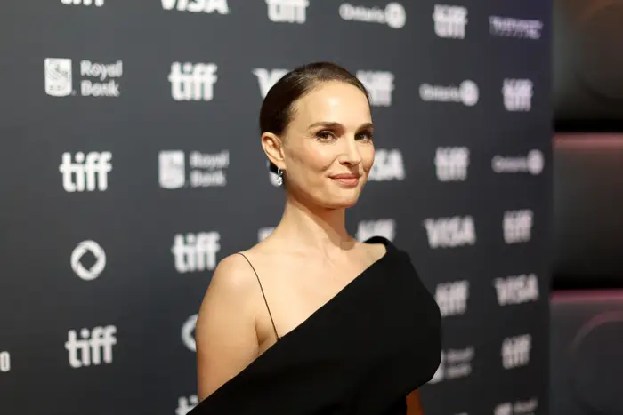En kvinne på den røde løperen i en en-skulder svart kjole på et filmfestival, poserer for bilder med sponsorlogoer i bakgrunnen