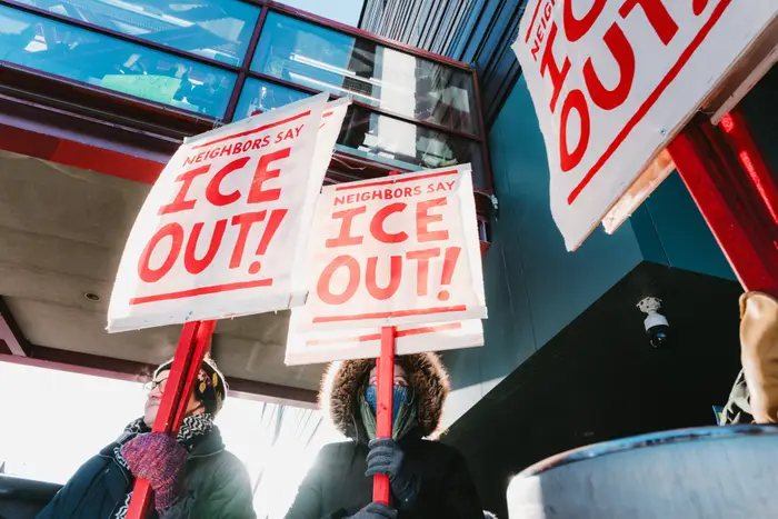Demonstranter holder skilt der det står ICE OUT utenfor en moderne bygning