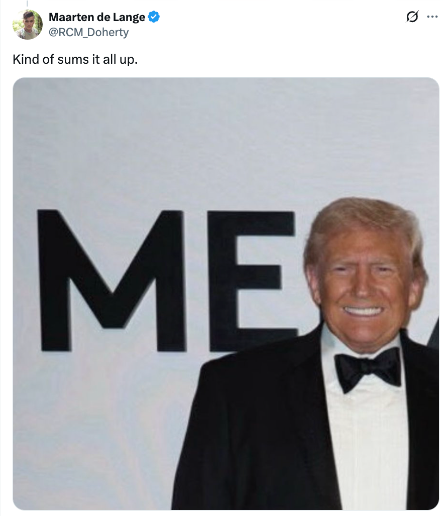 En mann i smoking smiler foran et delvis synlig skilt