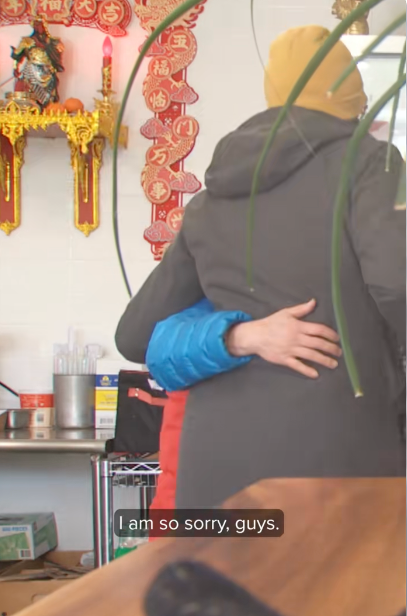 To personer som klemmer seg inne i et dekorert rom; den ene har på seg lue og jakke, den andre er i blå puffy jakke. Underteksten lyder: 