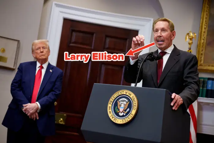 To menn på et podium i en formell setting. Den ene snakker i en mikrofon mens den andre står med hendene sammen