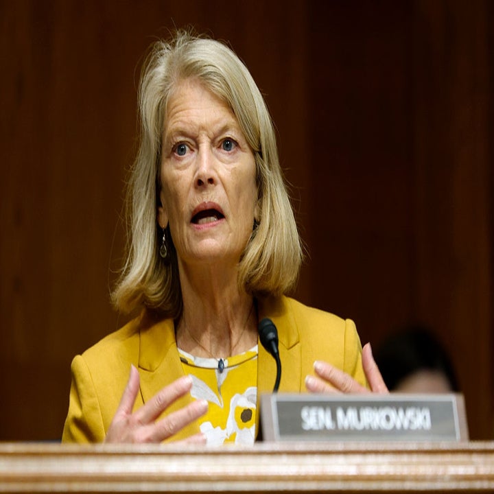 Kvinne i en blomstertopp og blazer snakker lidenskapelig bak en mikrofon og gestikulerer med hendene på en formell begivenhet