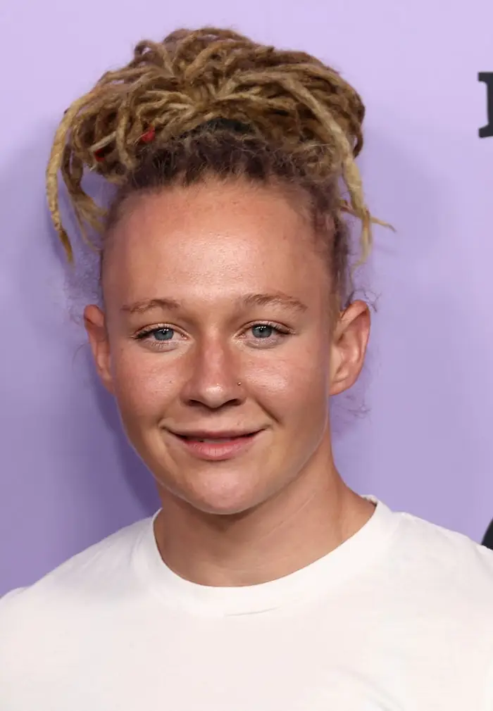 Person med dreadlocks og nesepiercing, iført en vanlig t-skjorte, smiler til kameraet mot en vanlig bakgrunn