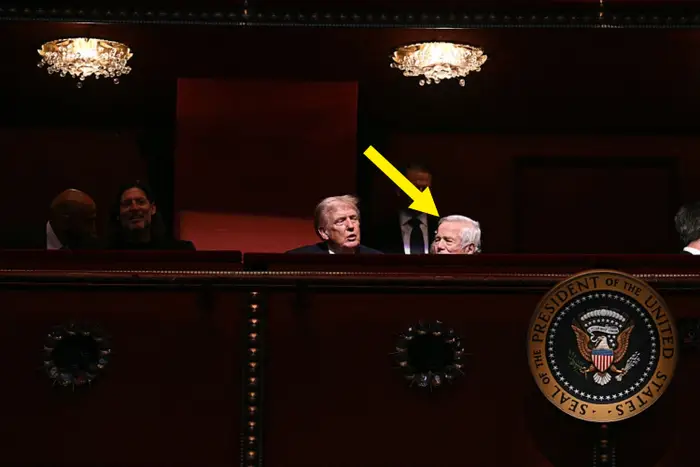 Gruppe mennesker på en teaterbalkong med den amerikanske presidentens segl synlig, noe som tyder på en fremtredende begivenhet. Setene har utsmykkede detaljer