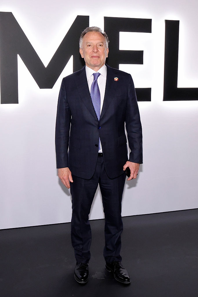 Person i formell blå dress og slips står foran et stort skilt ved et arrangement