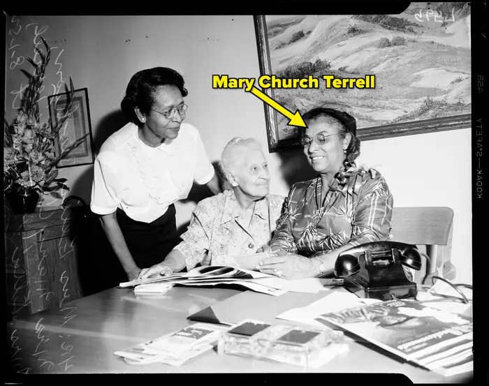 Tre kvinner sitter ved et bord, engasjert i samtale, med dokumenter og en telefon i nærheten. De ser ut til å gjennomgå materiell sammen