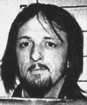 Jeg vet ikke hvem denne personen er, men en mann med skulderlangt hår og bart ser fremover med et nøytralt uttrykk i et svart-hvitt bilde