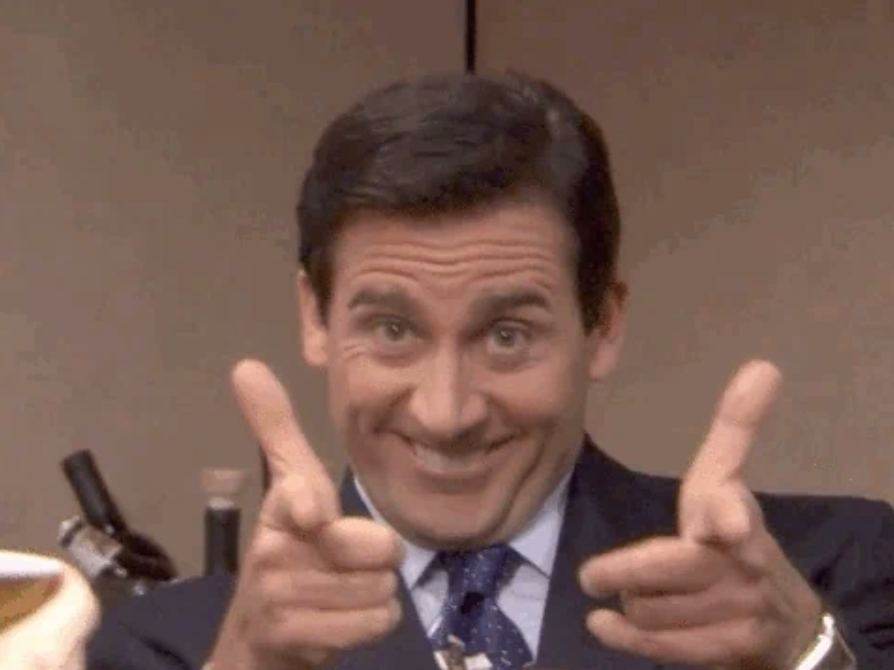 En mann i dress gliser og peker med fingervåpen, og formidler entusiasme eller oppmuntring på en arbeidsplass