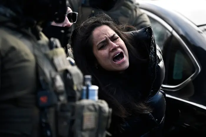 En kvinne blir arrestert av politifolk og uttrykker nød. Hun er ved siden av en bil, omgitt av offiserer i uniform og taktisk utstyr