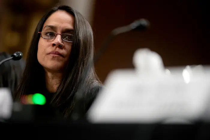 En person med briller snakker inn i en mikrofon ved det som ser ut til å være en formell hendelse eller hørselsinnstilling