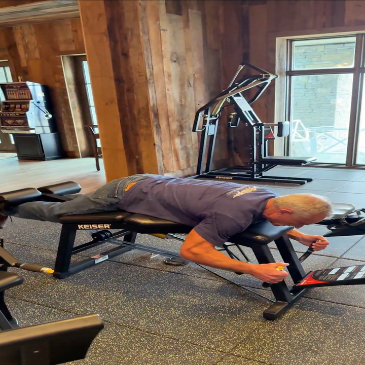 Mann på et treningsstudio som bruker en ryggforlengelsesmaskin, ser ut til å se på noe på gulvet