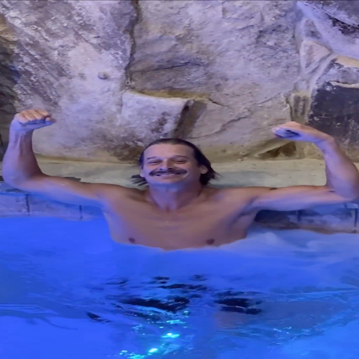 Person som smiler og bøyer muskler i en badestamp mot et steinete bakteppe