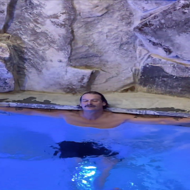 Person som slapper av i et basseng, lener seg mot en steinete vegg med et rolig uttrykk