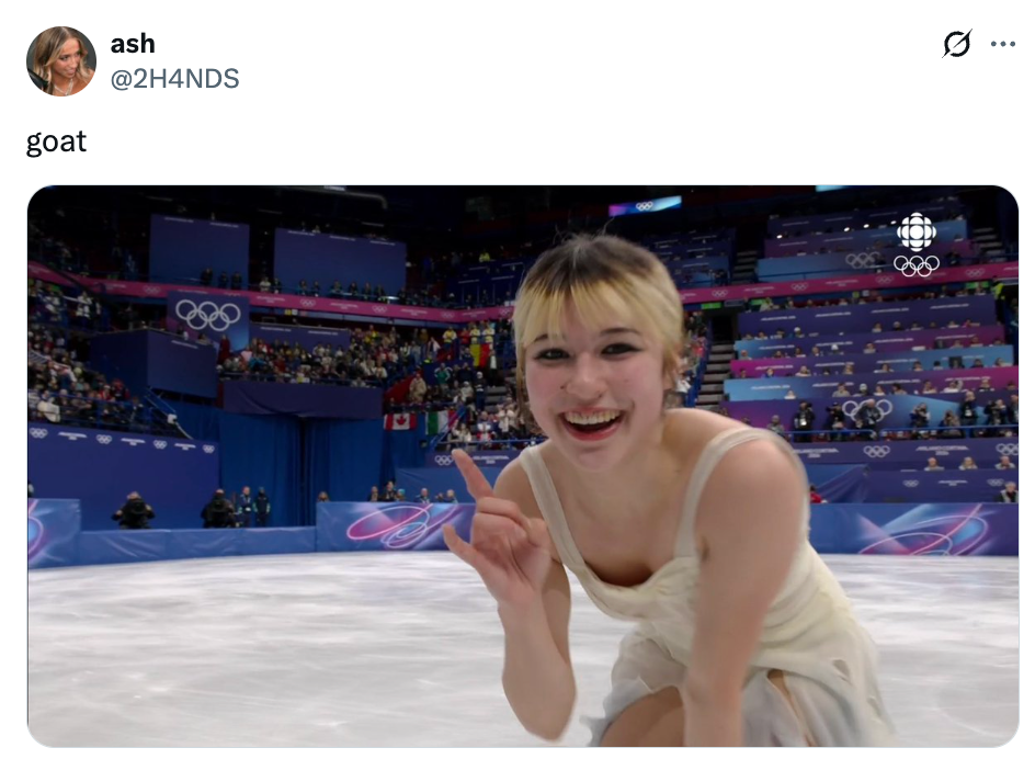 Kunstløper på is smiler og lager et fredstegn ved vinter-OL, iført en ermeløs kjole