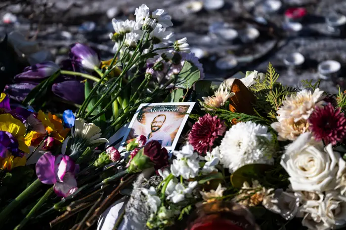 Blomsterhyllest med forskjellige blomster rundt et bilde av en person på et minnested. Stearinlys er synlige i bakgrunnen