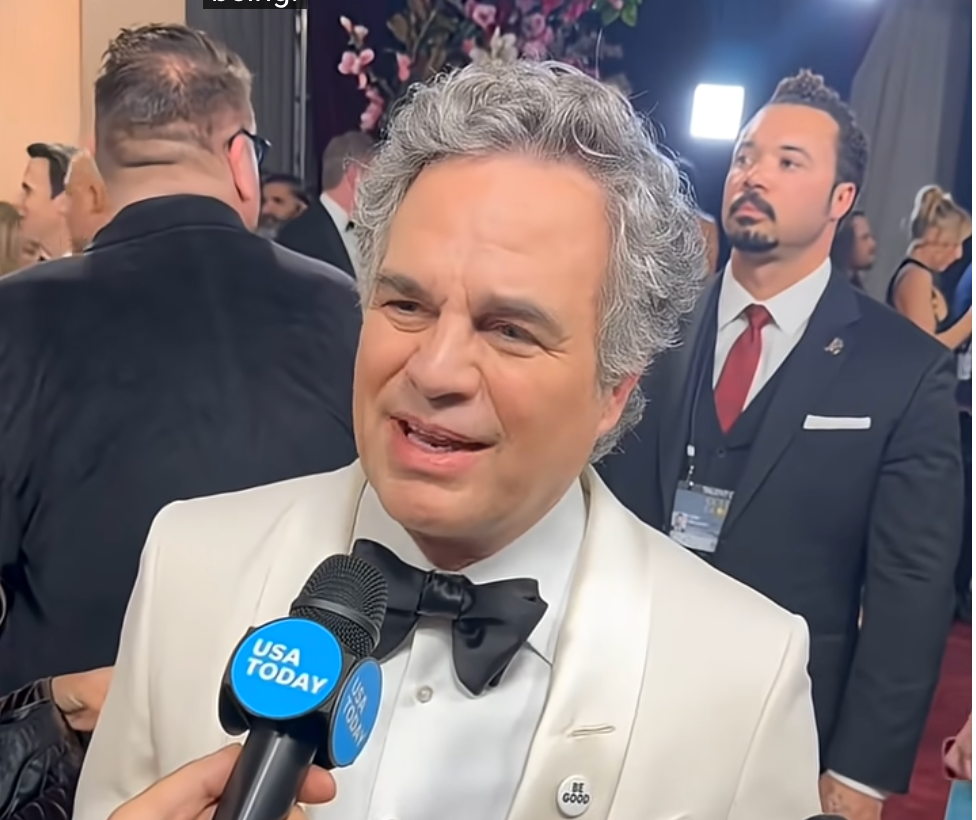 En person i hvit smoking snakker med en USA Today-reporter på et formelt arrangement med mennesker og kameraer i bakgrunnen