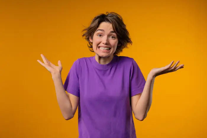 Person som trekker på skuldrene med et smil, iført en uformell t-skjorte, satt mot en vanlig bakgrunn