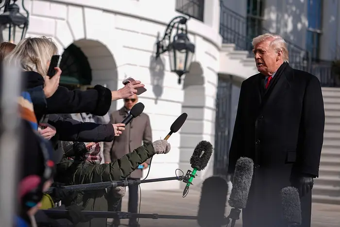 Person i mørk dress snakker med forsamlede journalister med mikrofoner utenfor en stor bygning