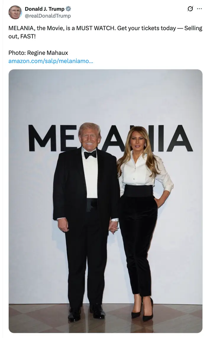 To personer står i høytidsklær. Man har på seg en svart smoking; den andre har på seg en hvit bluse og svarte bukser. Tekst fremmer "Melania, the Movie."