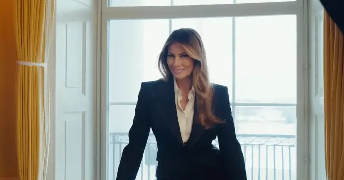 Person i skreddersydd dress står ved et stort vindu og smiler. Innstillingen virker elegant