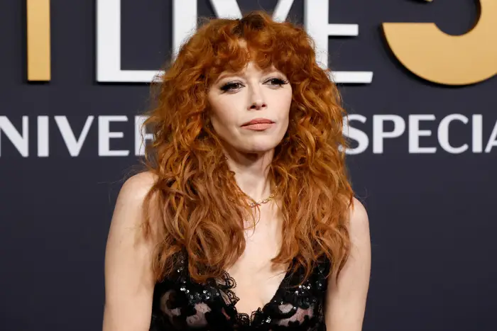 Natasha Lyonne med bølget hår i blondekjole poserer på et arrangement