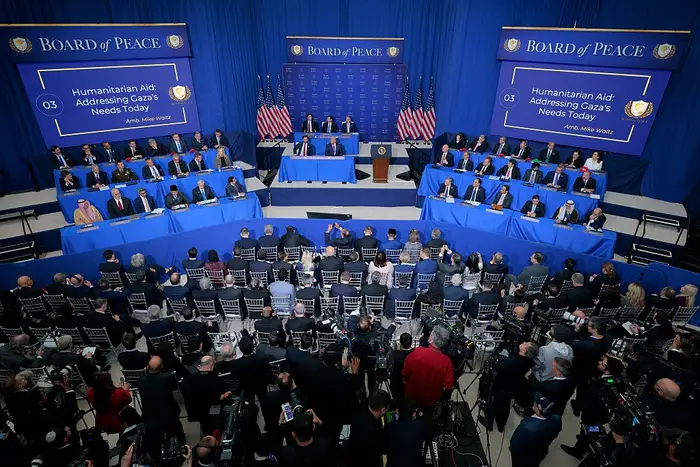 Bredbilde av et konferanserom med tjenestemenn på scenen som diskuterer humanitær hjelp. Publikum inkluderer mediepersonell, kameraer og deltakere