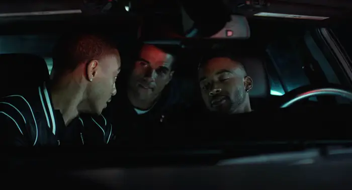 Tre menn sitter i en bil om natten og snakker