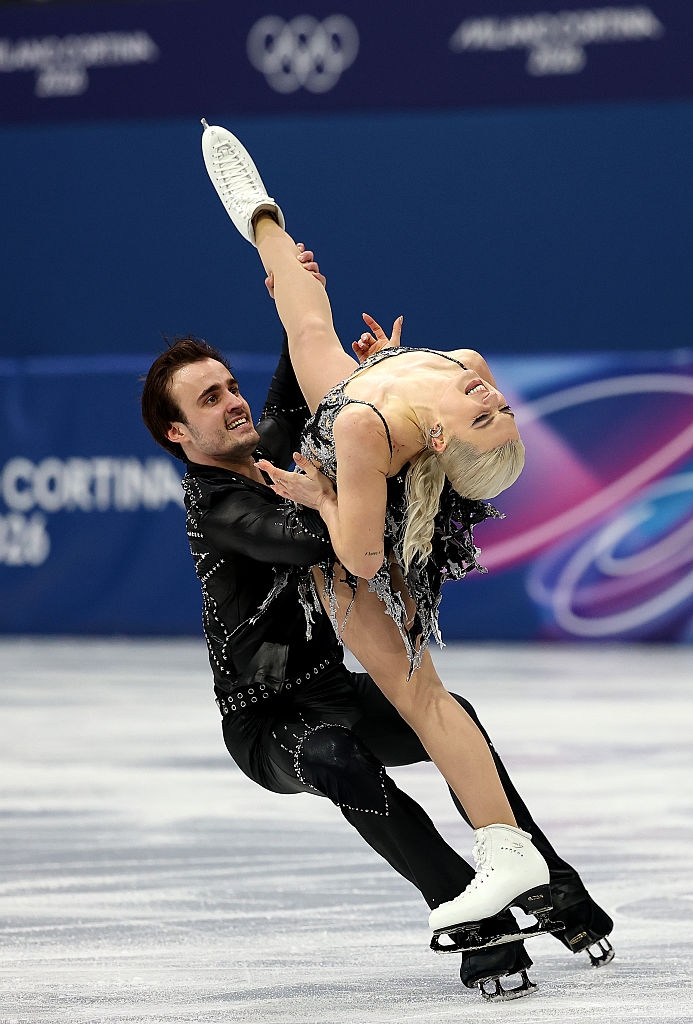 Et par kunstløpere som utfører et komplekst løft på en konkurranse, begge iført utsmykkede kostymer