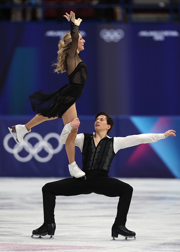 To kunstløpere utfører et intrikat løft på isen. Den kvinnelige skateren har på seg et flytende antrekk, og den mannlige skateren er i et montert ensemble