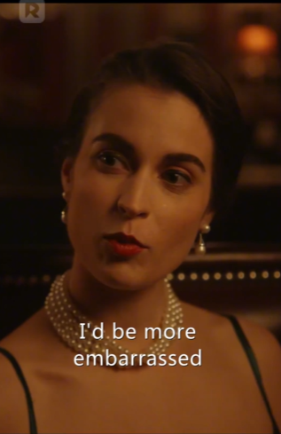 En kvinne med perlekjede snakker i et svakt opplyst miljø. Undertekstene sier: