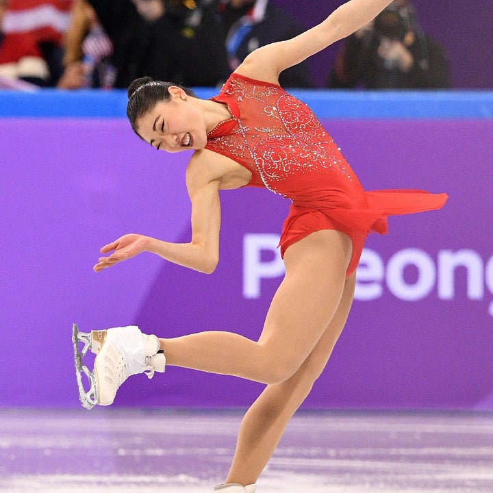 Kunstløper i en dynamisk positur på is, iført et elegant, tilpasset antrekk med intrikate detaljer. Publikum og amerikansk flagg er synlig i bakgrunnen