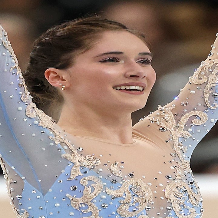 Kunstløper utstråler glede, iført et utsmykket, elegant kostyme med intrikate design, armene hevet i triumf