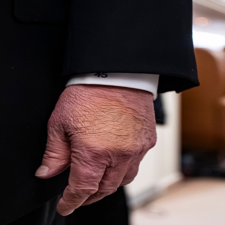 Persons hånd i formell drakt, sett fra siden, går gjennom en midtgang i det som ser ut til å være en flykabin