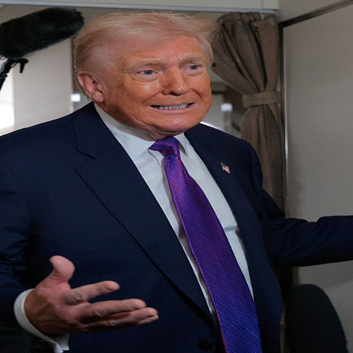 En person i dress og lilla slips snakker til noen utenfor kameraet og gestikulerer med en hånd, mens en annen person står i nærheten