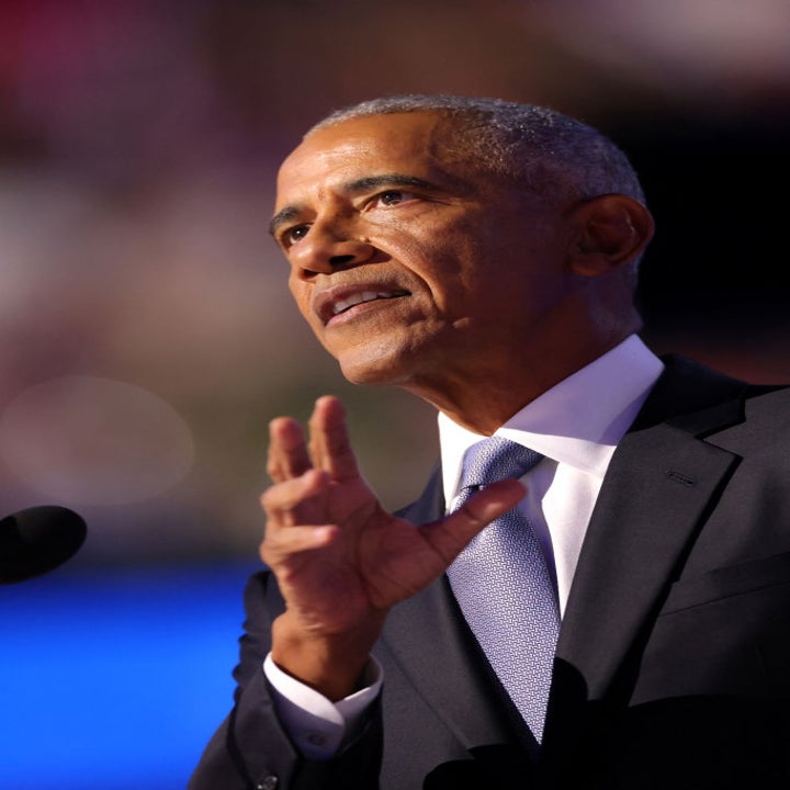 En dresskledd mann gestikulerer mens han snakker på et arrangement